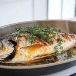 Black bass en train de cuire dans une poêle avec citron et herbes