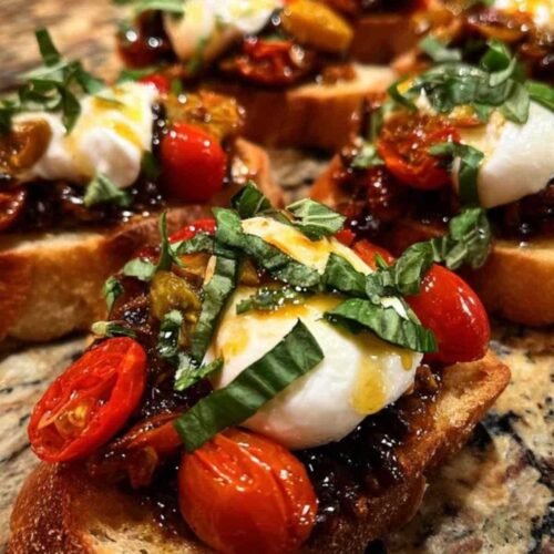 Plusieurs bruschettas à la tapenade, tomates confites et burrata, garnies de basilic frais et servies sur une planche en bois.