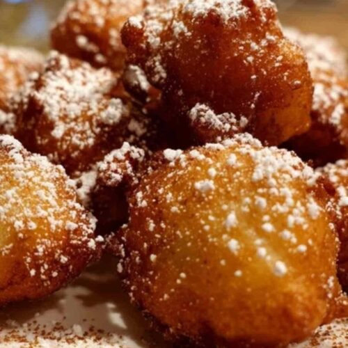 Une assiette de beignets aux pommes dorés et croustillants, généreusement saupoudrés de sucre et de cannelle.