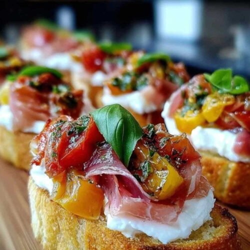 Plusieurs bruschettas à la burrata, tomates confites et jambon de Parme servies sur un plat en bois.