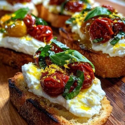 Plusieurs bruschettas à la burrata crémeuse, tomates confites et zeste de citron, servies sur une planche en bois.