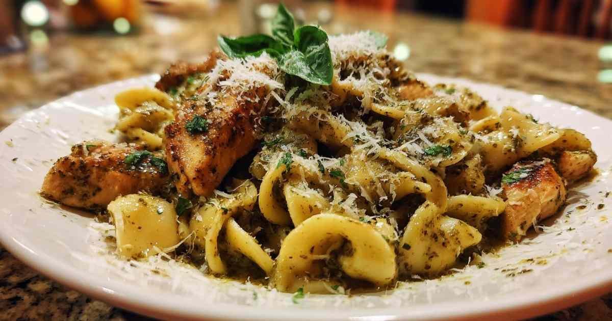 Ingrédients pour la recette de pâtes au poulet et pesto étalés sur un plan de travail en bois.