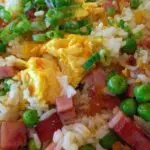 Un bol de riz cantonnais maison fumant, garni d'oignon vert frais, avec des baguettes posées à côté.