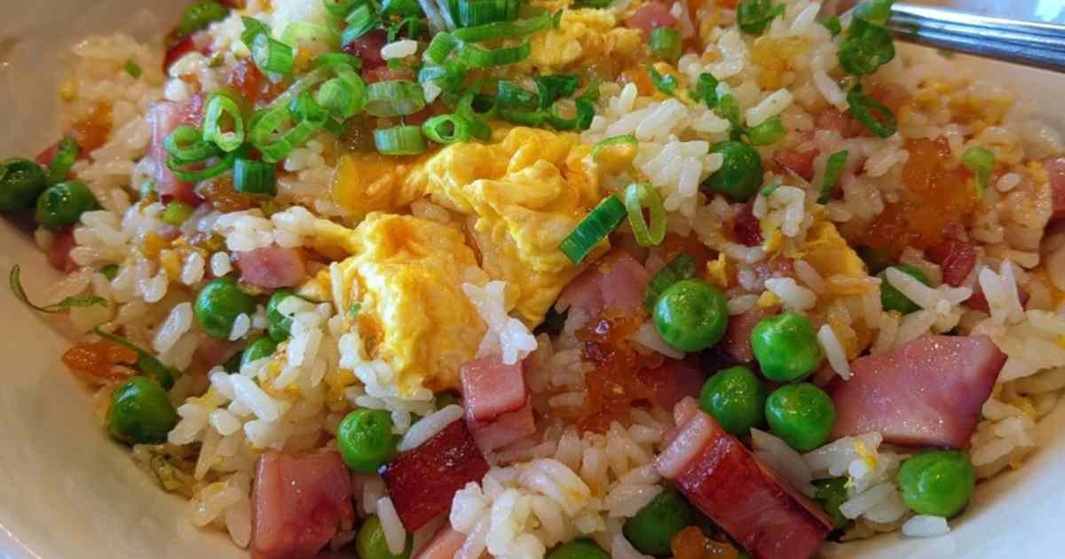 Un bol de riz cantonnais maison fumant, garni d'oignon vert frais, avec des baguettes posées à côté.