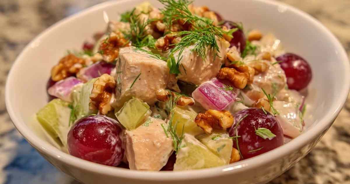  Salade de poulet aux raisins frais et noix servie dans un grand bol blanc, décorée d'aneth frais.