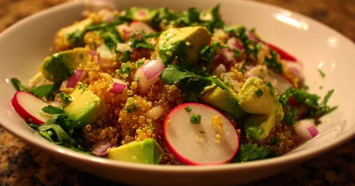 Main en train de verser le jus de citron vert sur les ingrédients de la salade de quinoa dans un saladier.