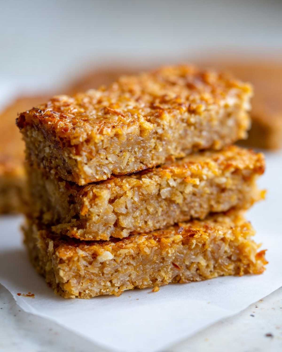 Gros plan de trois barres coco low-carb empilées, avec une texture croustillante et des flocons de noix de coco visibles.