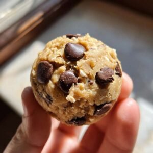Gros plan d'une bouchée de cookie dough au yaourt grec, parsemée de pépites de chocolat, tenue dans une main.