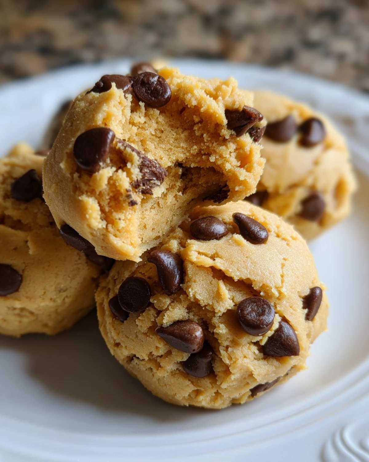 Gros plan de bites cookie dough au yaourt grec parsemées de pépites de chocolat sur une assiette blanche.