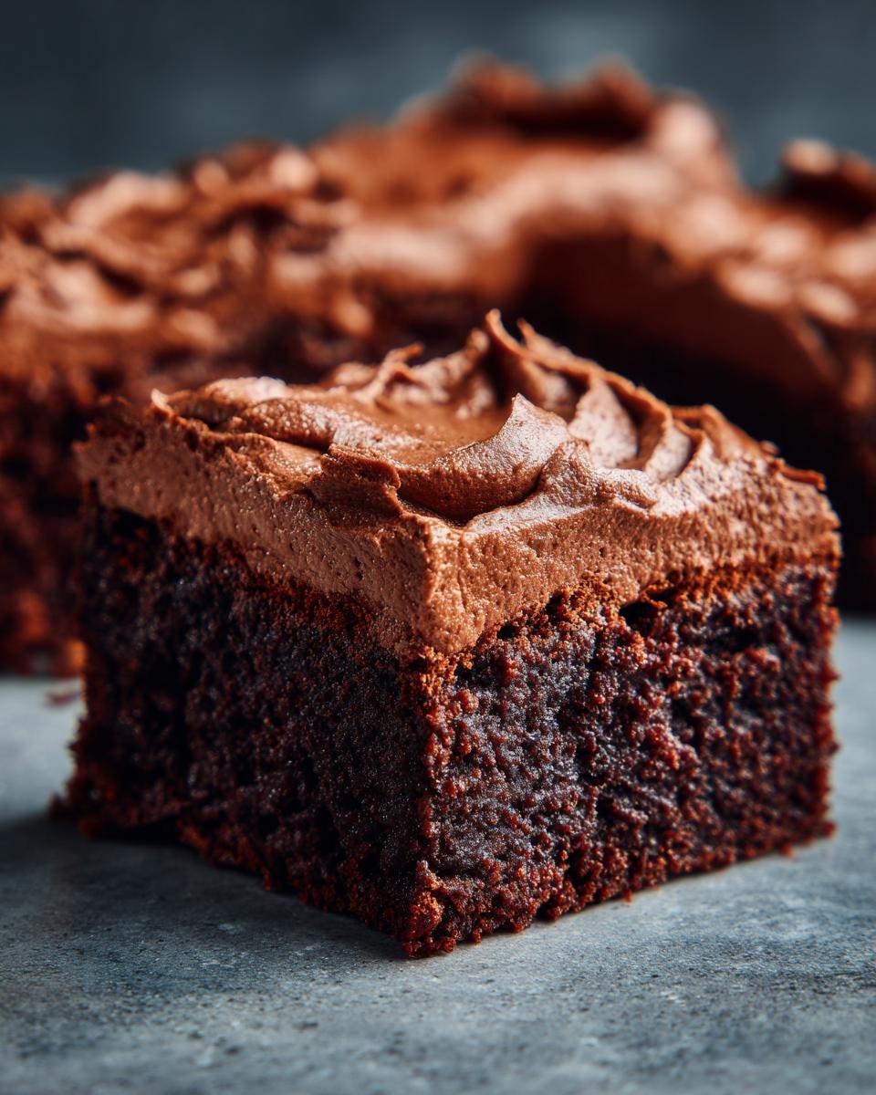 Gros plan d'une tranche de Brownies Mousse Chocolat, avec un glaçage onctueux au chocolat.