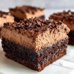Gros plan sur une tranche de Brownies Mousse Chocolat, avec une base de brownie dense et une couche aérienne de mousse au chocolat, saupoudrée de copeaux de chocolat.