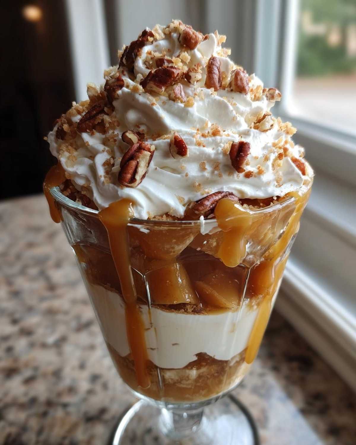 Gros plan d'une coupe dessert pomme caramel avec crème fouettée, noix et coulis de caramel.