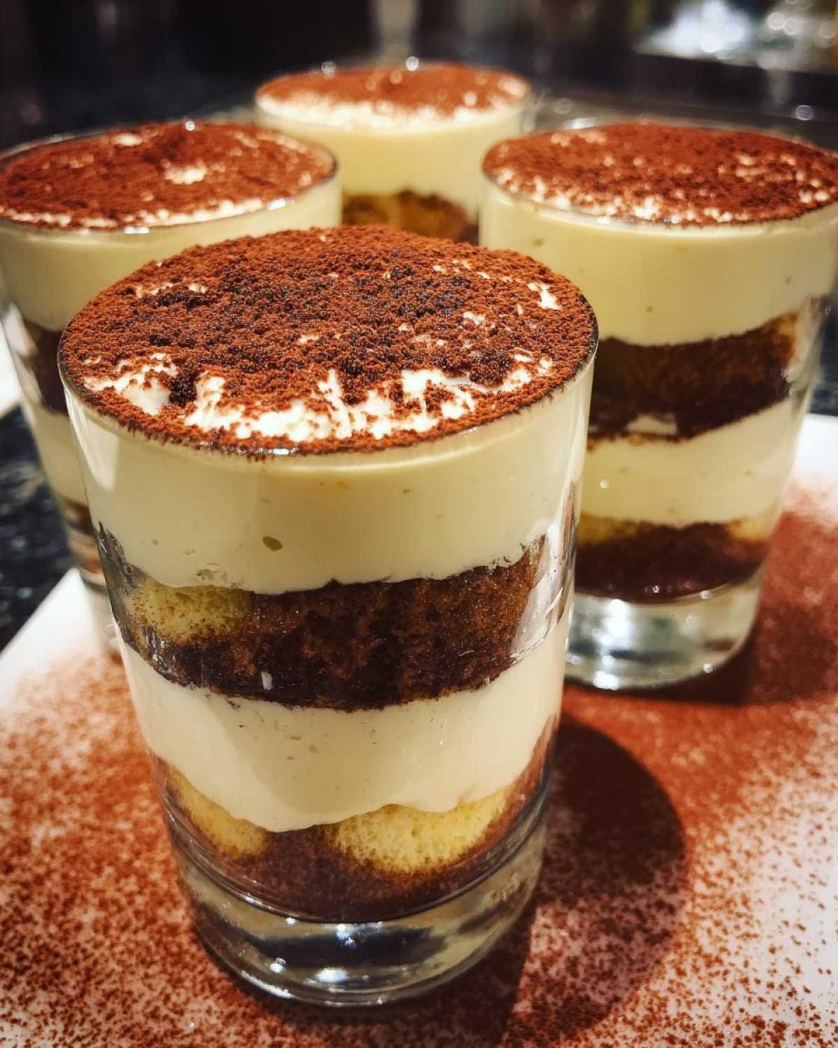 Gros plan sur des coupes tiramisu aux biscuits, superposées de crème et saupoudrées de cacao.