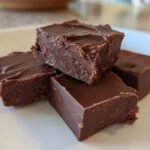 Gros plan de carrés de fudge keto 3 ingrédients au chocolat sur une assiette blanche.