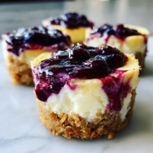 Gros plan sur des mini cheesecakes aux myrtilles et citron, garnis d'une compotée de myrtilles.