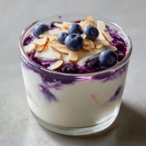 Gros plan d'une mousse cottage cheese myrtilles crémeuse, garnie de myrtilles fraîches et d'amandes effilées.