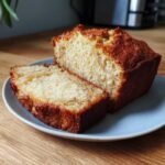 Une tranche de pain à la banane moelleux sur une assiette bleue, avec le reste du pain à côté.