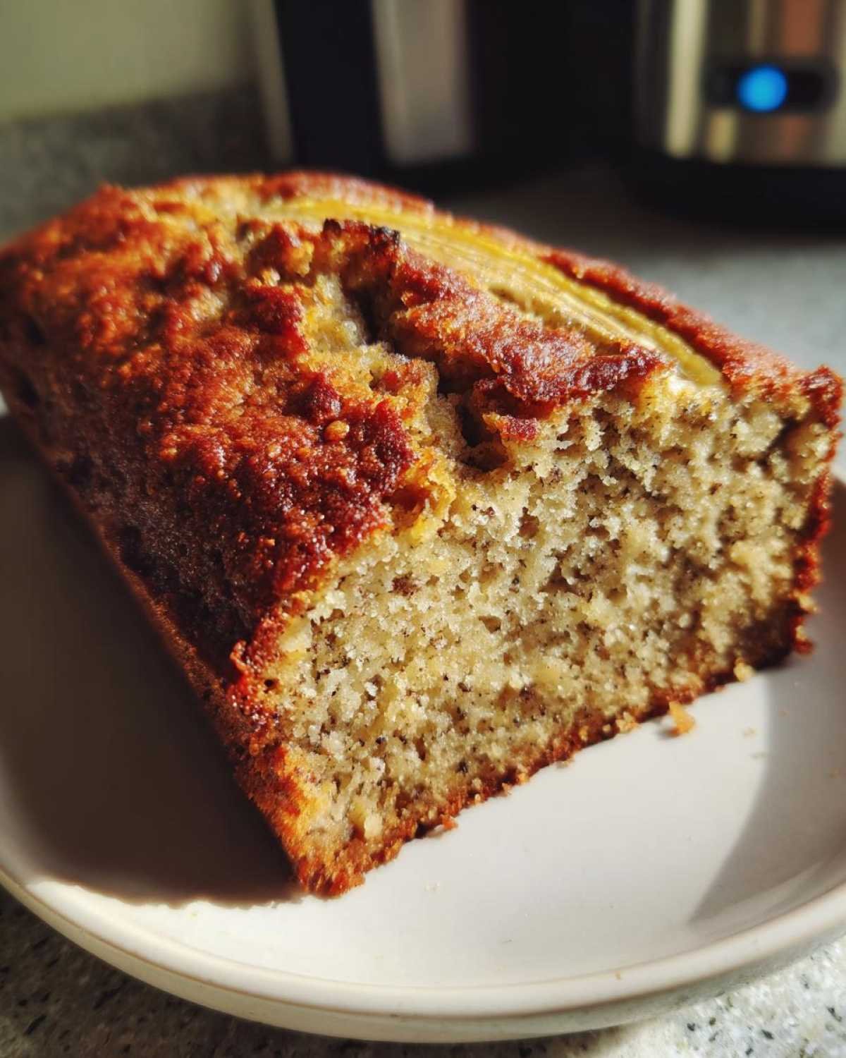 Gros plan sur une tranche de pain à la banane moelleux, avec des morceaux de banane visibles.