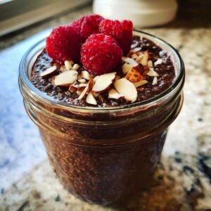 Gros plan d'un pudding chia chocolat protéiné dans un pot, garni de framboises et d'amandes effilées.