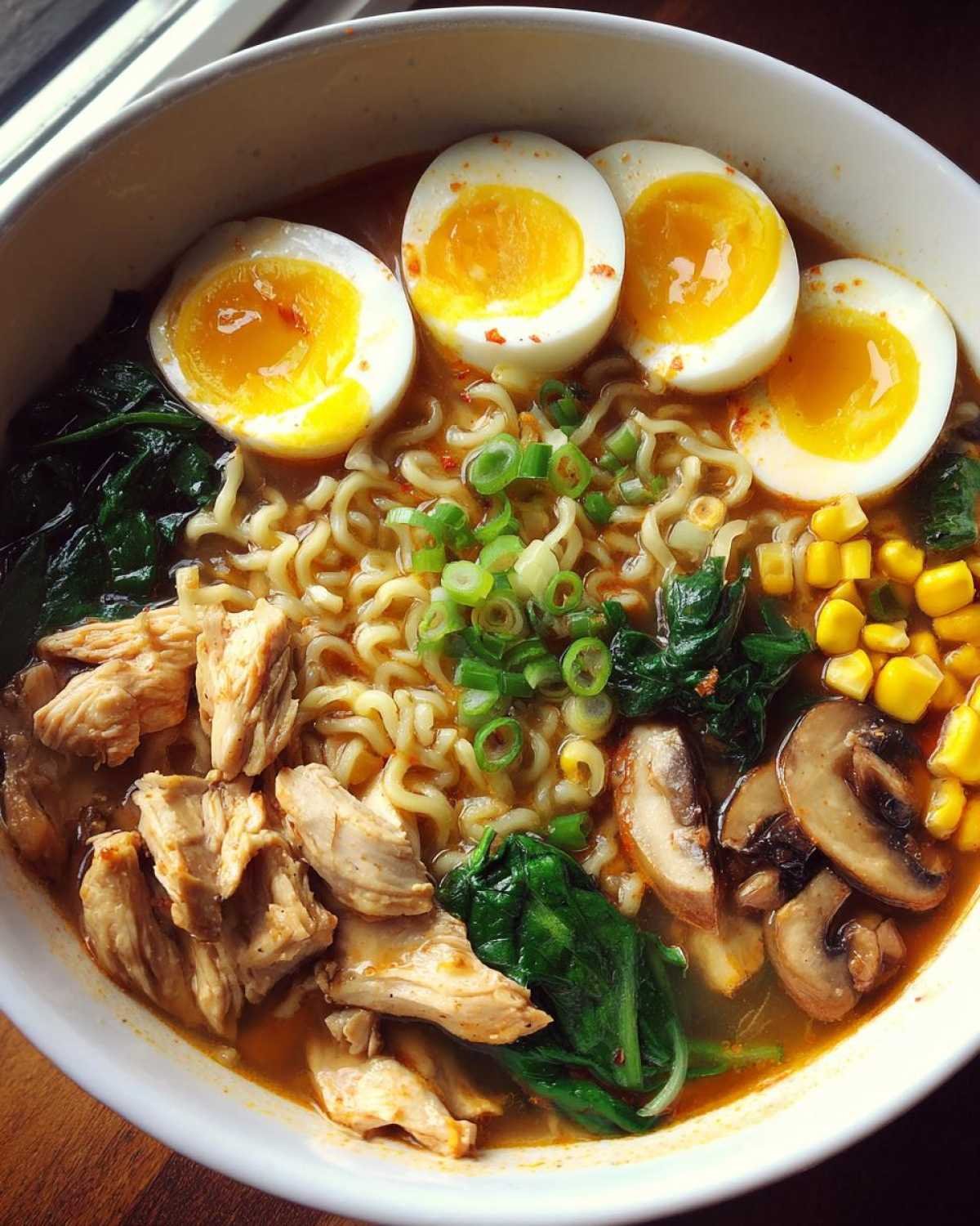 Gros plan sur un bol de soupe ramen facile avec des nouilles, du poulet effiloché, des œufs mollets, des épinards, du maïs et des champignons.