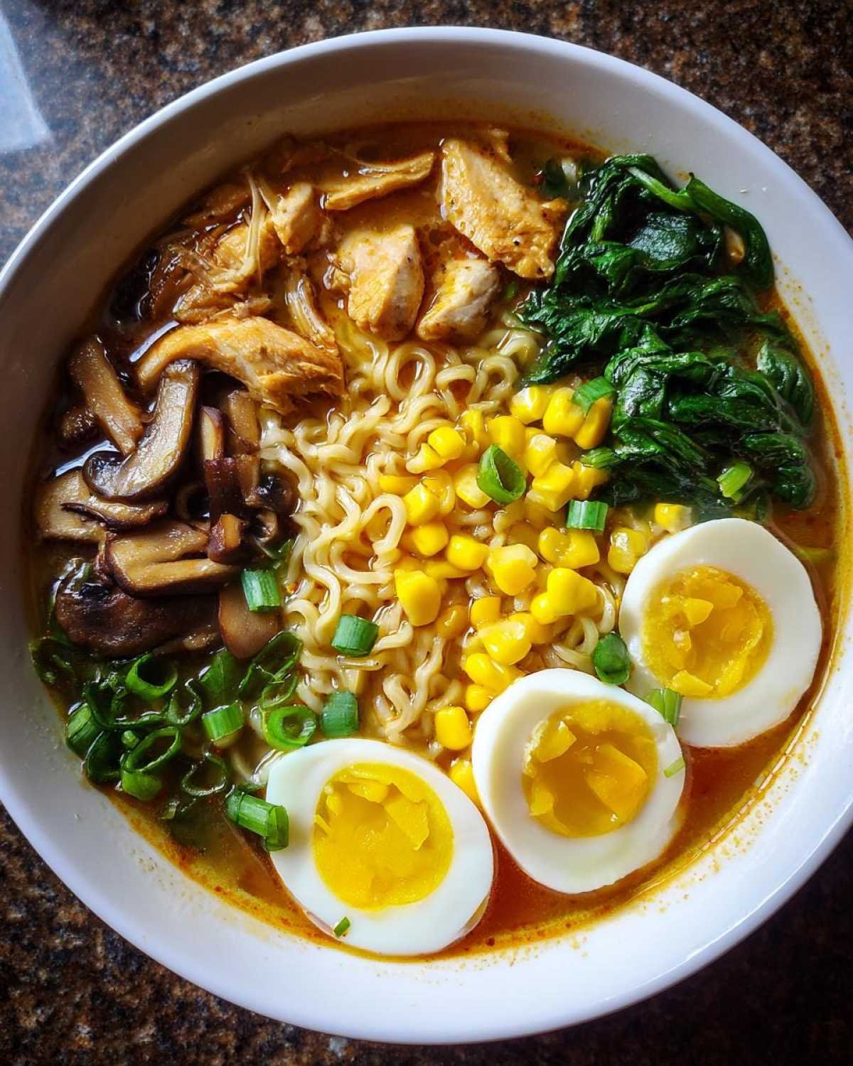 Gros plan d'une Soupe Ramen Facile dans un bol, garnie de poulet, d'œufs durs, de maïs, de champignons et d'épinards.