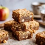 Gros plan sur une pile de blondies aux pommes et érable, parsemés de morceaux de fruits et de noix.