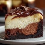 Gros plan d'une tranche de brownie cheesecake avec des couches de chocolat et de crème, garnie de chocolat.