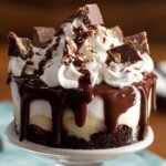 Gros plan d'un Cheesecake Brownie Sundae avec crème fouettée, sauce chocolat et morceaux de brownie.