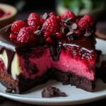 Une part de cheesecake chocolat noir framboise sur une assiette blanche, garnie de framboises fraîches et de copeaux de chocolat.