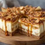 Gros plan d'une tranche de cheesecake aux pommes caramel salé, nappé de caramel coulant et garni de miettes et de morceaux de pomme.