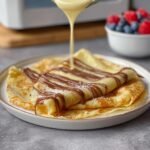 Gros plan sur des crêpes faciles au mixeur garnies de sauce au chocolat et saupoudrées de sucre glace.