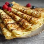 Gros plan de crêpes faciles au mixeur roulées et garnies de chocolat fondu, de framboises et de myrtilles.