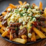 Gros plan de frites au fromage et steak, garnies de fromage émietté et de persil frais.