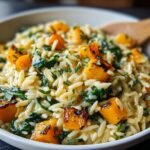 Gros plan d'un bol d'orzo crémeux butternut épinards, garni de persil frais.