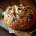 Gros plan d'un pain artisanal à l'ail rôti et romarin, doré et croustillant, sur une planche en bois.