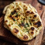 Gros plan d'un pain naan au levain jeté doré et garni de persil frais, sur une planche en bois.