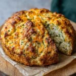 Gros plan d'un pain soda au cheddar et herbes fraîchement cuit, avec une tranche coupée.