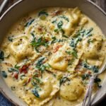 Gros plan d'une Soupe Crémeuse aux Raviolis, avec des raviolis dorés dans une sauce onctueuse, garnie d'épinards et de tomates séchées.