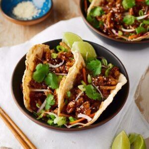 Gros plan sur deux tacos au poulet teriyaki garnis de coriandre fraîche, d'oignons verts et de graines de sésame.