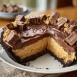 Gros plan d'une tarte au beurre de cacahuète Reese's coupée, garnie de morceaux de bonbons et de chocolat.
