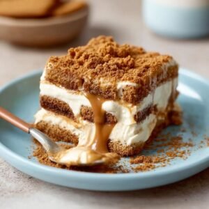 Une part de Tiramisu Biscoff Spéculoos crémeux, garnie de miettes de biscuits et de coulis de caramel.