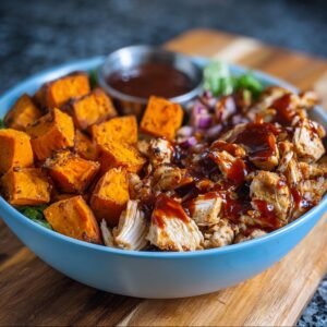 Gros plan d'un bol de poulet BBQ et patates douces, garni de sauce BBQ et d'oignons rouges.
