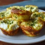 Gros plan de bouchées aux œufs et fromage cottage garnies d'herbes fraîches, sur une assiette blanche.
