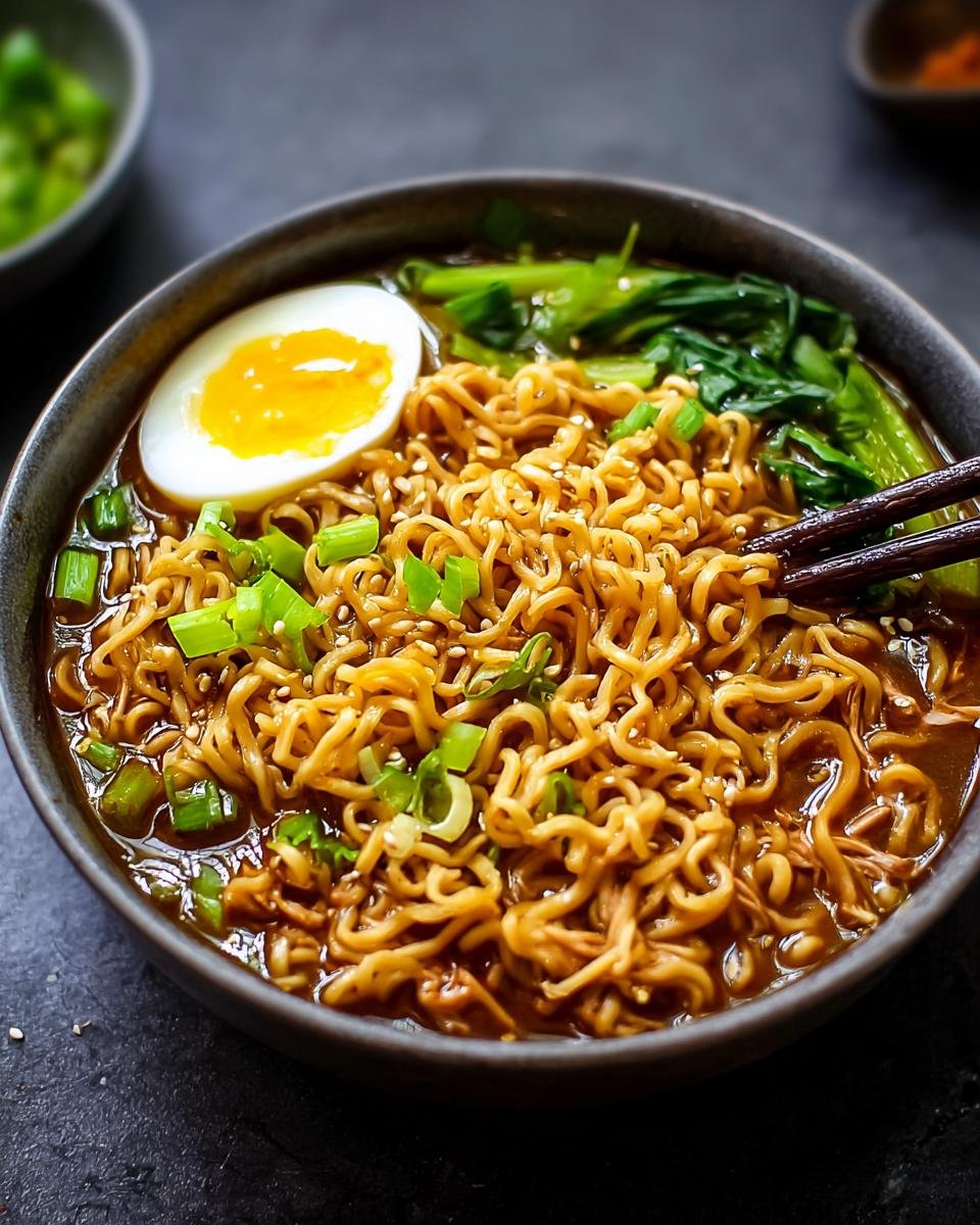 Gros plan d'un bol de nouilles ramen protéinées faciles avec un œuf mollet, des oignons verts et des légumes verts.