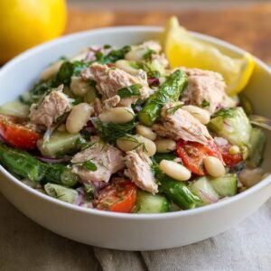 Gros plan d'une salade de thon et haricots blancs avec des tomates, concombres et herbes fraîches, garnie d'un quartier de citron.