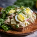 Gros plan d'une tranche de pain grillé garnie d'une généreuse portion de salade de thon et œufs, décorée d'œufs durs et d'aneth.