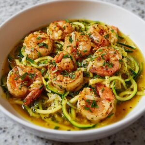 Gros plan de crevettes scampi sur un lit de zoodles, garnies d'herbes fraîches.